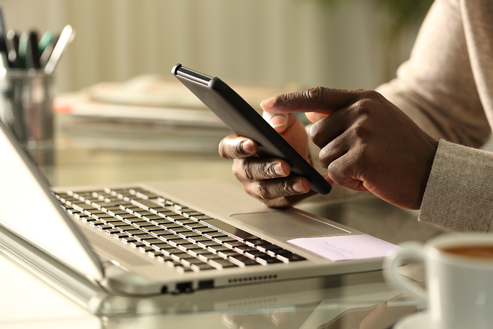 photo of hands operating a cell phone while sitting in front of a laptop