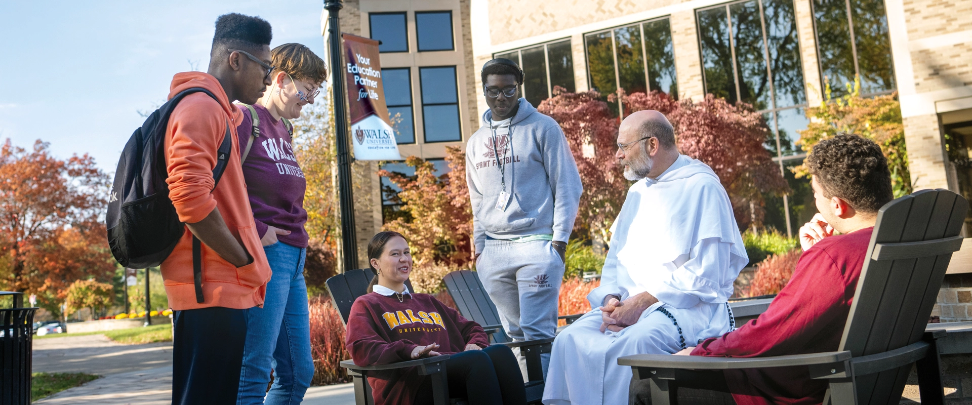 photo of a group of students and the University Chaplain seated by the Alumni fire pit